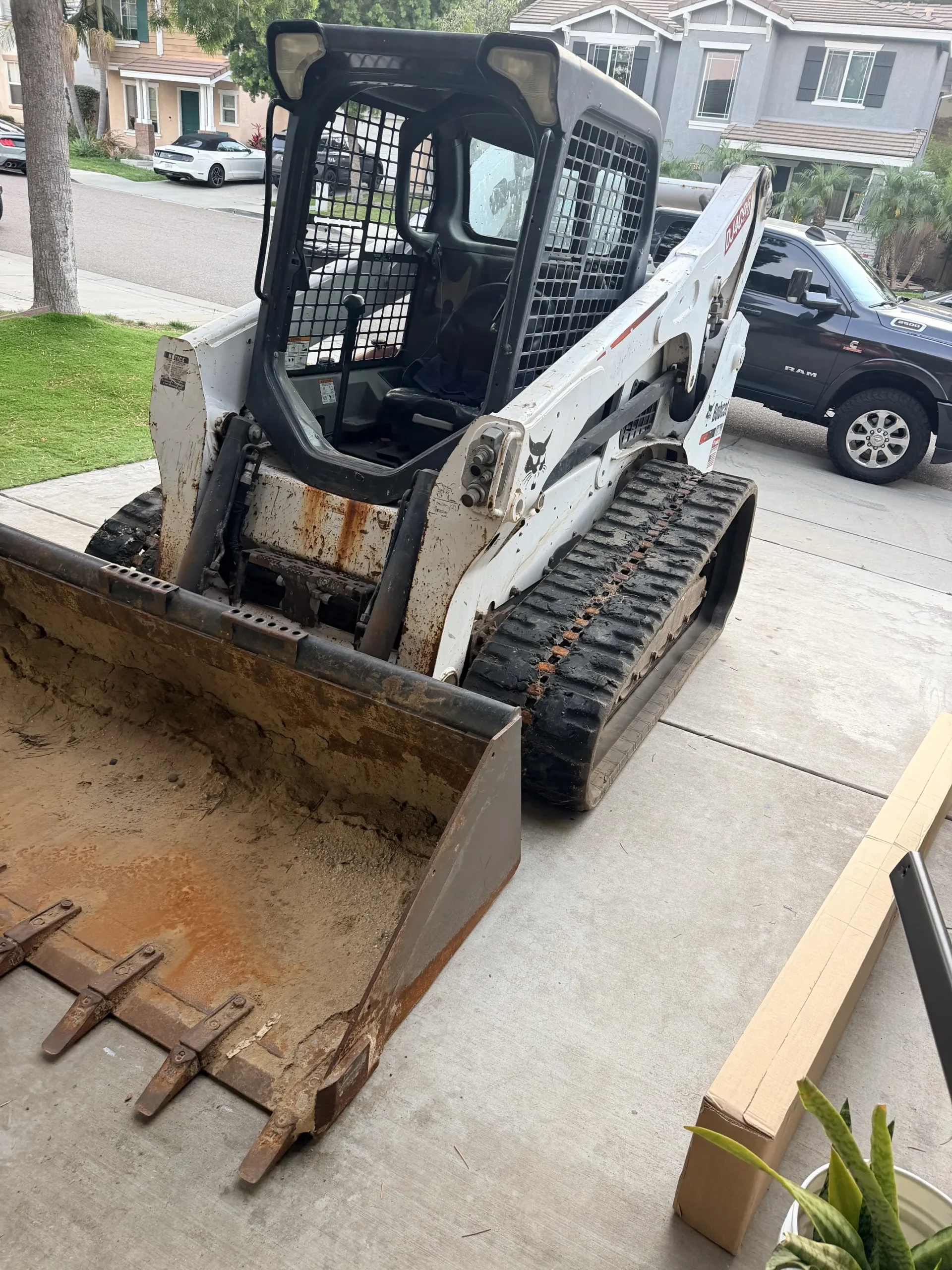 Bobcat T770 skid steer with a full bucket of dirt during a residential driveway cleanup in San Diego